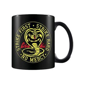 Taza negra con el emblema de Cobra Kai y las frases "Strike First, Strike Hard, No Mercy".