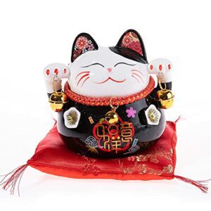 Figura de gato de la suerte Maneki Neko de porcelana negra decorativa sobre un cojín rojo.